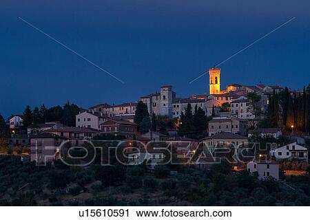 Stock Image - Twilight view of medieval hilltop town of MonteCastello di Vibio. stone houses and belltower, olive groves on slope below, with pink and blue twilight sky, Umbria, Italy. Fotosearch