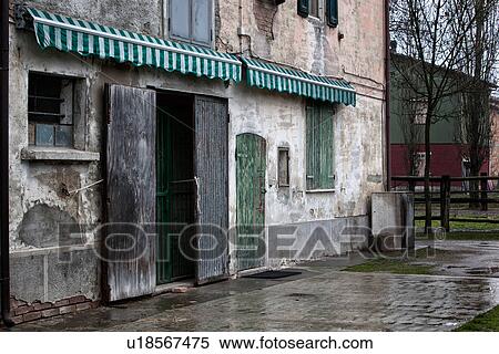 View of old stucco house with crumbling facade, Door with wooden shutters half open, green wooden shutter over window and storage door, with green and white awning, all paint peeling, other houses beyond, typical style, Emilia Romagna, Italy View Large Photo Image Stock Photography - View of old stucco house with crumbling facade, Door with wooden shutters half open, green wooden shutter over window and storage door, with green and white awning, all paint peeling, other houses beyond, typical style, Emilia Romagna, Italy. Fotosearch