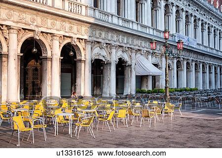 Stock Photography - View of one person sitting in the open cafe of the Piazzetta at dawn, empty yellow chairs, Archaeology Museum building in background, Venice, Italy. Fotosearch
