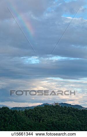 View of Todi hilltop town with bank of trees in foreground, hills beyond, and dramatic billowing grey-blue clouds with rainbow, Umbria, Italy View Large Photo Image Picture - View of Todi hilltop town with bank of trees in foreground, hills beyond, and dramatic billowing grey-blue clouds with rainbow, Umbria, Italy. Fotosearch