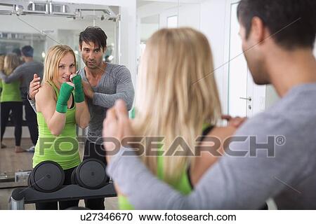 Stock Image - Boxer practicing with trainer in gym. Fotosearch