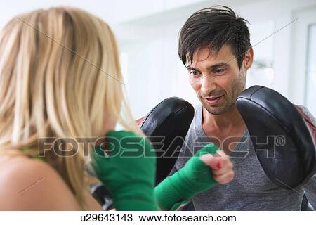 Stock Image - Boxer practicing with trainer in gym. Fotosearch