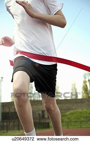 Stock Image - Boy breaking finish line tape on track. Fotosearch