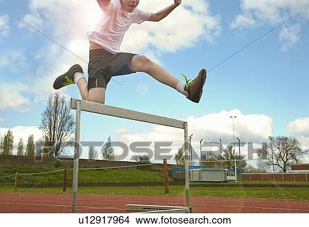 Picture - Boy jumping over hurdle on track. Fotosearch