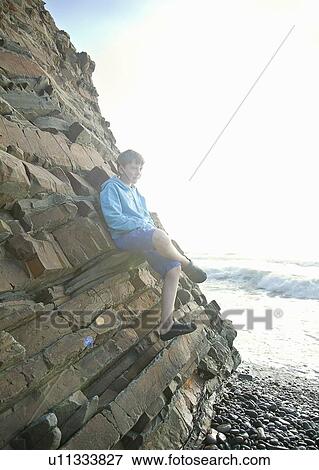 Boy leaning on rock formation on beach View Large Photo Image Stock Photo - Boy leaning on rock formation on beach. Fotosearch