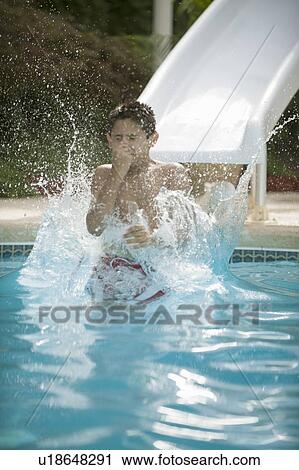 Stock Image - Boy on water slide splashing into pool. Fotosearch