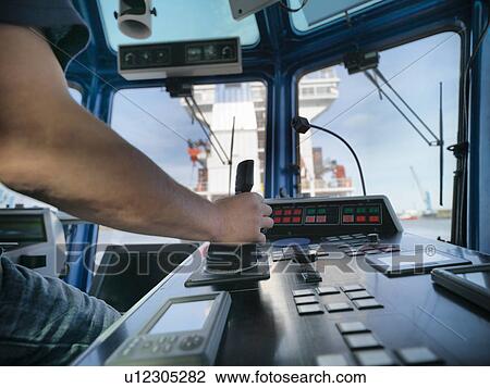 Stock Image - Captain steering tugboat in wheelhouse. Fotosearch
