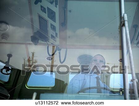 Stock Image - Captain steering tugboat in wheelhouse. Fotosearch