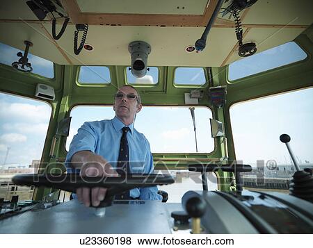 Stock Photo - Captain steering tugboat in wheelhouse. Fotosearch