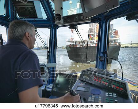 Stock Photography - Captain steering tugboat in wheelhouse. Fotosearch