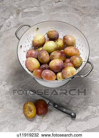 Stock Image - Close up of plums in colander. Fotosearch