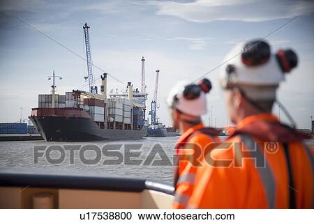 Stock Image - Container ship sailing into urban harbor. Fotosearch
