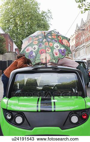 Couple balancing umbrella on car roof View Large Photo Image Stock Image - Couple balancing umbrella on car roof. Fotosearch
