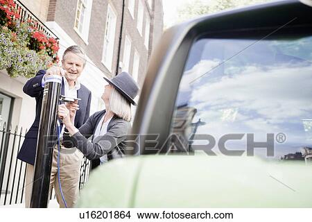 Couple charging electric car on street View Large Photo Image Picture - Couple charging electric car on street. Fotosearch