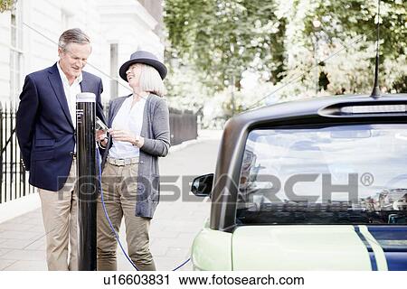 Couple charging electric car on street View Large Photo Image Stock Image - Couple charging electric car on street. Fotosearch