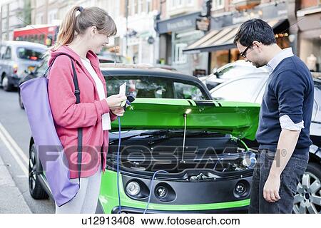 Couple charging electric car on street View Large Photo Image Stock Photo - Couple charging electric car on street. Fotosearch