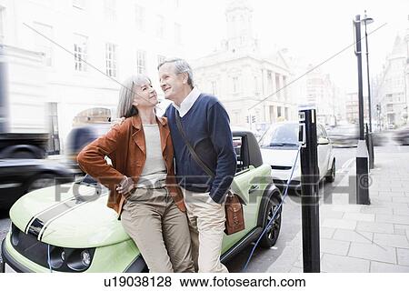 Couple charging electric car on street View Large Photo Image Stock Photo - Couple charging electric car on street. Fotosearch