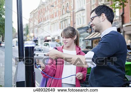 Couple charging electric car on street View Large Photo Image Stock Photo - Couple charging electric car on street. Fotosearch