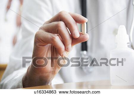 Stock Image - Doctor holding pill in office. Fotosearch