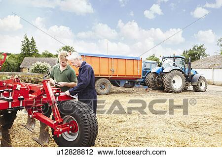 Farmers adjusting machinery in field View Large Photo Image Stock Image - Farmers adjusting machinery in field. Fotosearch