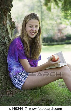 Girl eating apple and reading in park View Large Photo Image Stock Photo - Girl eating apple and reading in park. Fotosearch