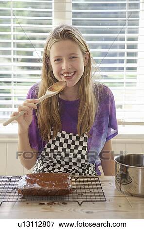 Girl tasting cake frosting in kitchen View Large Photo Image Stock Photo - Girl tasting cake frosting in kitchen. Fotosearch