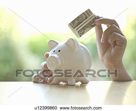 Stock Image - Hang putting dollar bill in piggy bank. Fotosearch