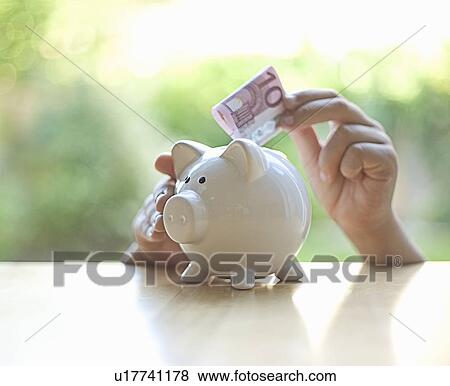 Stock Photo - Hang putting Euro note in piggy bank. Fotosearch