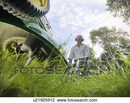Stock Image - Low angle view of man mowing lawn. Fotosearch