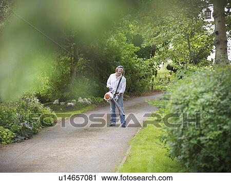 Stock Image - Man blowing leaves on paved road. Fotosearch