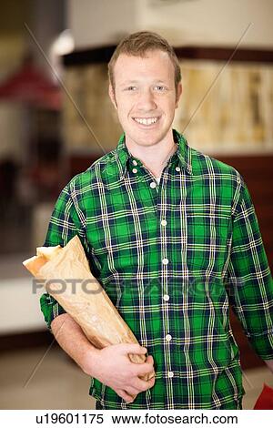Stock Photography - Man carrying baguette in grocery store. Fotosearch