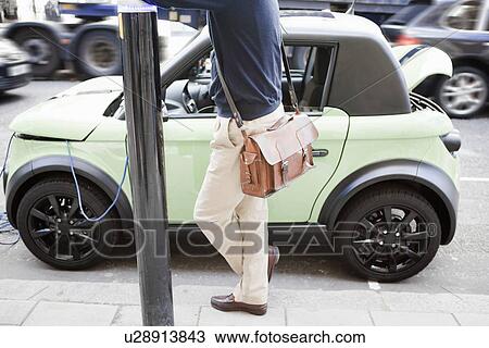 Man charging electric car on city street View Large Photo Image Stock Image - Man charging electric car on city street. Fotosearch