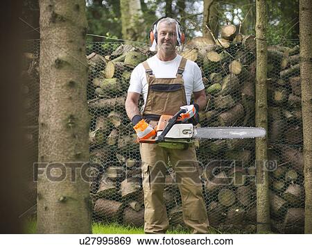 Man holding chain saw by firewood View Large Photo Image Stock Photo - Man holding chain saw by firewood. Fotosearch