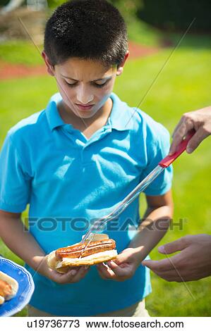 Stock Image - Man serving son hot dog outdoors. Fotosearch