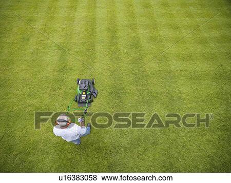 Stock Photo - Man wearing headphones and mowing lawn. Fotosearch