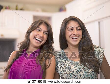 Stock Photo - Sisters laughing together in kitchen. Fotosearch
