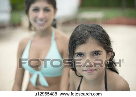 Stock Photo - Sisters sitting by swimming pool. Fotosearch