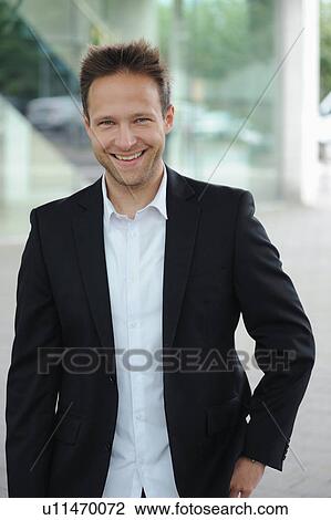 Stock Image - Smiling businessman standing at window. Fotosearch