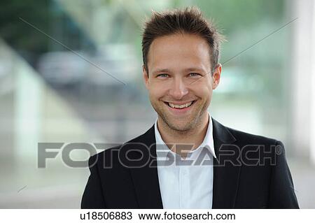 Stock Image - Smiling businessman standing at window. Fotosearch