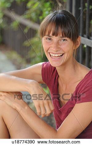 Stock Image - Smiling woman sitting on ground. Fotosearch