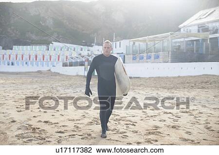Stock Image - Surfer carrying board on beach. Fotosearch