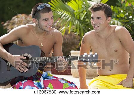 Stock Image - Teenage boys relaxing by swimming pool. Fotosearch