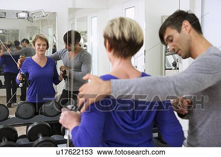 Stock Image - Trainer adjusting woman’s form in gym. Fotosearch