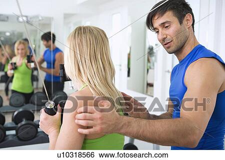 Stock Photograph - Trainer adjusting woman’s form in gym. Fotosearch