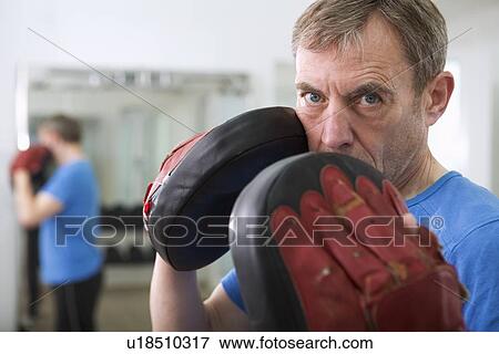 Stock Photo - Trainer wearing padded gloves in gym. Fotosearch