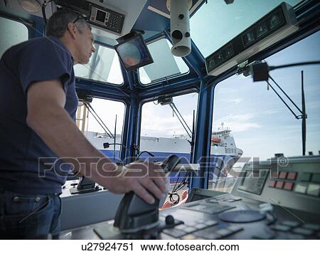 Stock Image - Tugboat captain steering in wheelhouse. Fotosearch