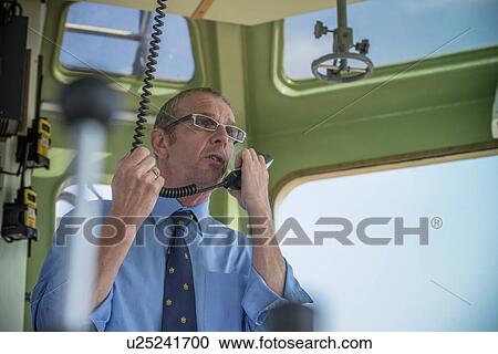 Stock Image - Tugboat captain talking on walkie talkie. Fotosearch