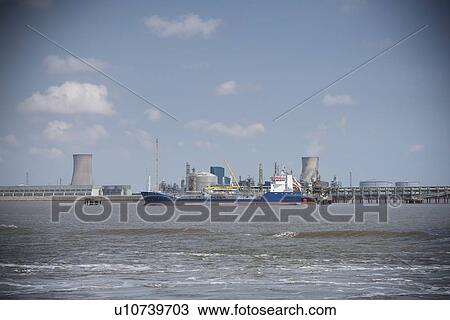 Stock Image - Tugboat pulling ship in urban harbor. Fotosearch