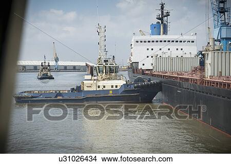 Tugboat pushing ship in urban harbor View Large Photo Image Picture - Tugboat pushing ship in urban harbor. Fotosearch