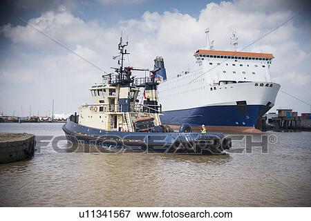 Tugboat sailing in urban harbor View Large Photo Image Stock Photo - Tugboat sailing in urban harbor. Fotosearch